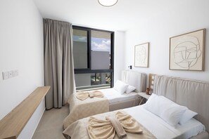 Ein Hotelzimmer mit zwei Betten, einem Fenster mit Vorhängen, einem Nachttisch und einem Bild an der Wand.