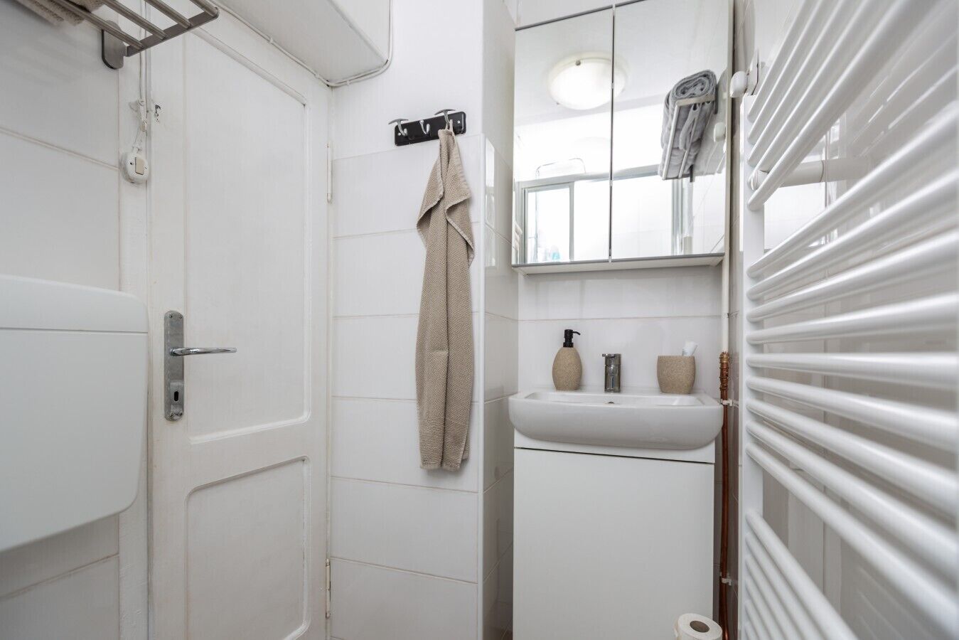 A bathroom with a white door, a towel hanging on a rack, a sink with a soap dispenser, and a toilet.