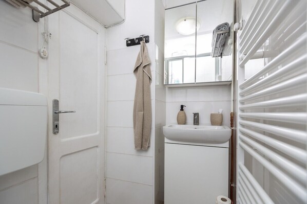 Ein Badezimmer mit einer weißen Tür, einem Handtuch auf einem Haken, einem Waschbecken mit Seifenspender und einer Toilette.