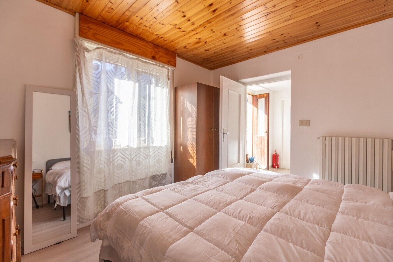 Een slaapkamer met een groot bed, houten plafond en een deur naar een andere kamer.