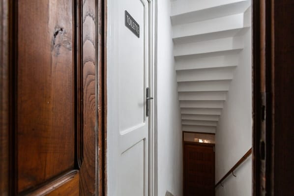 A wooden door with a sign reading 'TOILETTE' and a white interior staircase leading to a lower level.