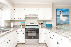 A modern kitchen with white cabinets, a stainless steel range, and a painting of a woman by the sea. - Big Fish - Classic 4BR Oceanfront Home - Covered Porch (Topsail Beach)