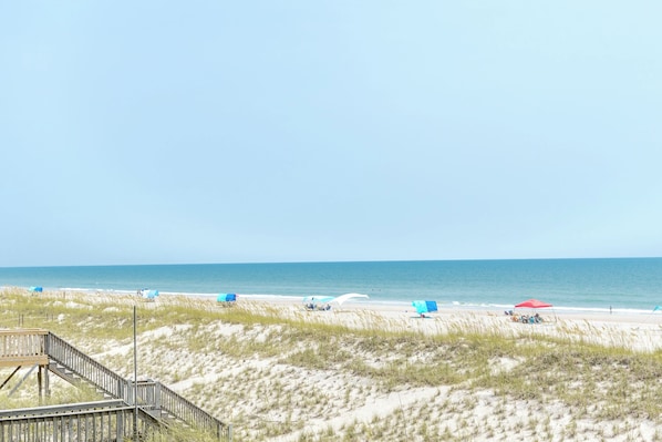 A beach with a wooden boardwalk leading to the shore, sandy dunes, and beach umbrellas. - Big Fish - Classic 4BR Oceanfront Home - Covered Porch (Topsail Beach)