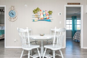 A dining area with a white table and four chairs, a wall clock, and a decorative sailboat mural. - Big Fish - Classic 4BR Oceanfront Home - Covered Porch (Topsail Beach)