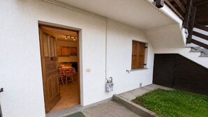 A residential property with a covered patio, a small garden, and a kitchen visible through an open door.