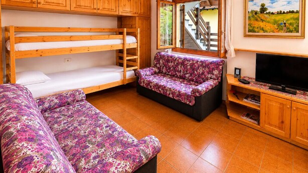 A room with bunk beds, a sofa, a TV, and a painting.