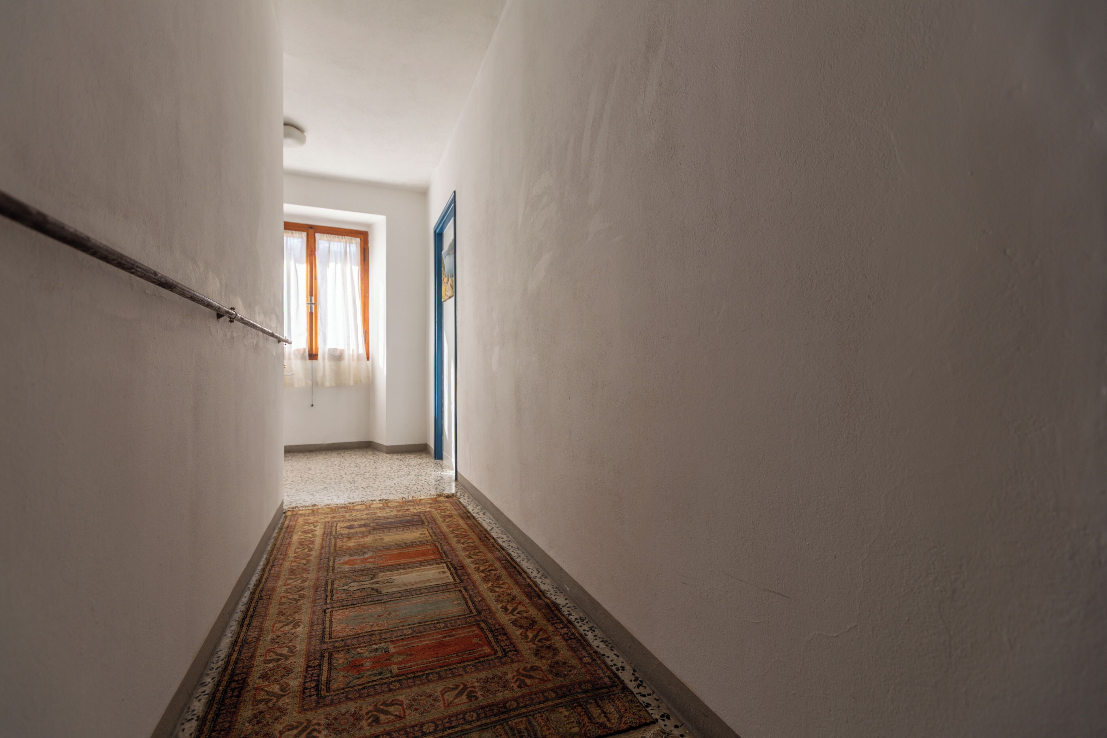 Un couloir étroit, orné d’un tapis à motifs, avec des murs blancs et une porte au fond.