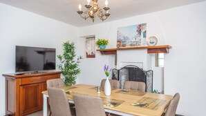 A dining area with a wooden table, chairs, a television on a cabinet, a potted plant, and a painting on the wall.