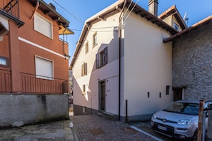 A narrow street with buildings on either side, a parked car, and cobblestone pavement. - Casa Klaus (Occagno)