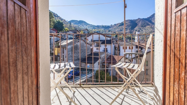 A balcony with a metal railing, a view of a mountainous landscape, and buildings in the background.