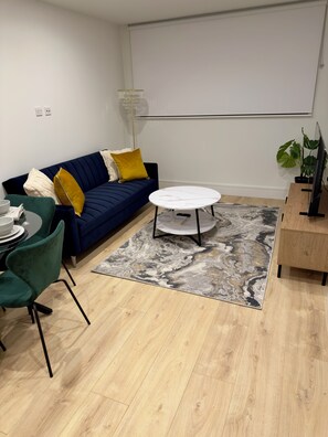 Un salon moderne avec un canapé bleu, une table basse ronde et un coin repas agrémenté d’une chaise verte.