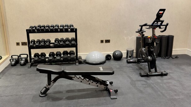 Ein Fitnessraum mit Langhantelbank, Kurzhanteln, Hanteltrainer und Yogamatte.