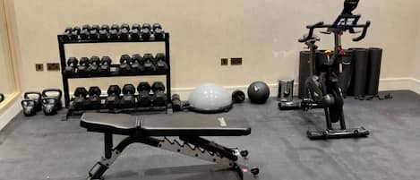 Une salle de sport équipée d’un banc de développé couché, d’haltères, d’un vélo d’appartement et d’un tapis de yoga.