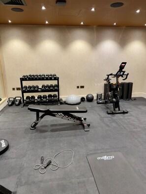 A gym with a bench press, dumbbells, a stationary bike, and a yoga mat. - 1 Luxury 1-Bed | Sleeps 4 | Free Parking, Gym, Cinema, Games Room, Lounge + More (London)