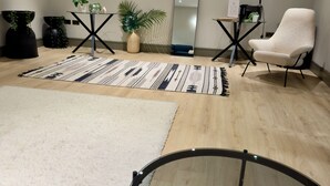 Ein modernes Wohnzimmer mit einem runden Glastisch, einem weißen Sessel, einem großen Spiegel und einem schwarzen Beistelltisch mit Pflanze.