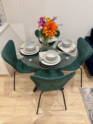 Uma mesa de vidro redonda com pratos e tigelas brancos, rodeada por cadeiras estofadas verdes.