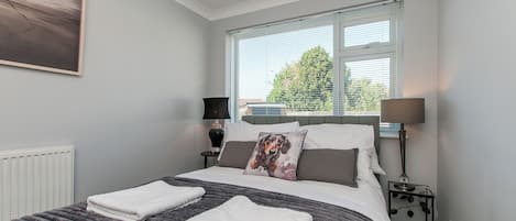 A neatly made bed with two towels, a window with blinds, and a lamp on a bedside table.