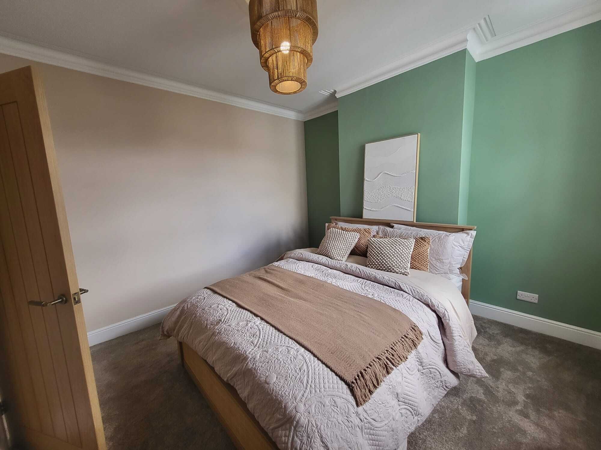 A bedroom with a bed, a wooden door, a green wall, and a ceiling light fixture.