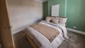 A bedroom with a bed, a wooden door, a green wall, and a ceiling light fixture.
