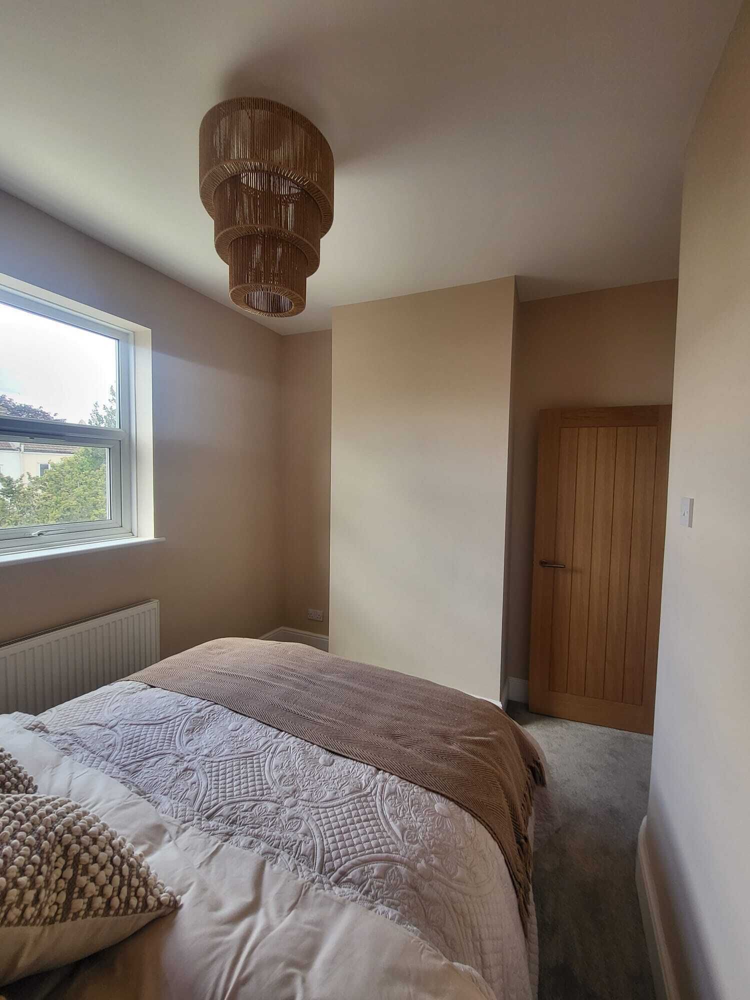 Un dormitorio con cama, ventana, puerta y lámpara en el techo.