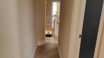 Un pasillo con un patrón de suelo tipo espiga que conduce a una escalera y una habitación con una puerta oscura.