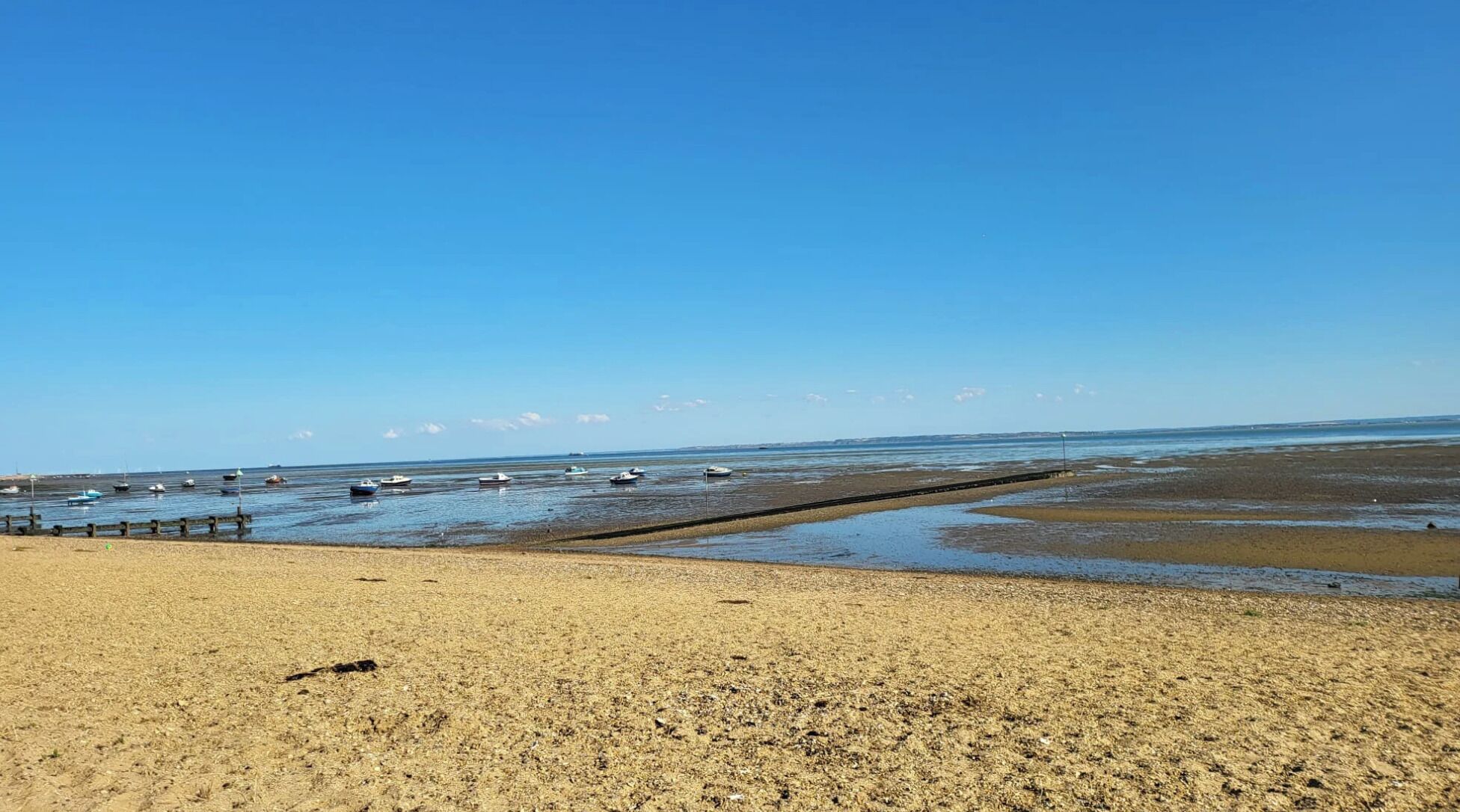 Una playa con barcos, un muelle de madera y cielo despejado.
