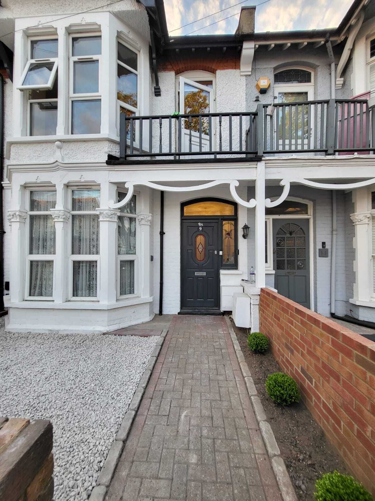 A two-story house with a front entrance, a balcony, and a gravel pathway leading to the door.