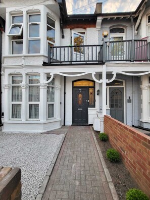 A two-story house with a front entrance, a balcony, and a gravel pathway leading to the door.