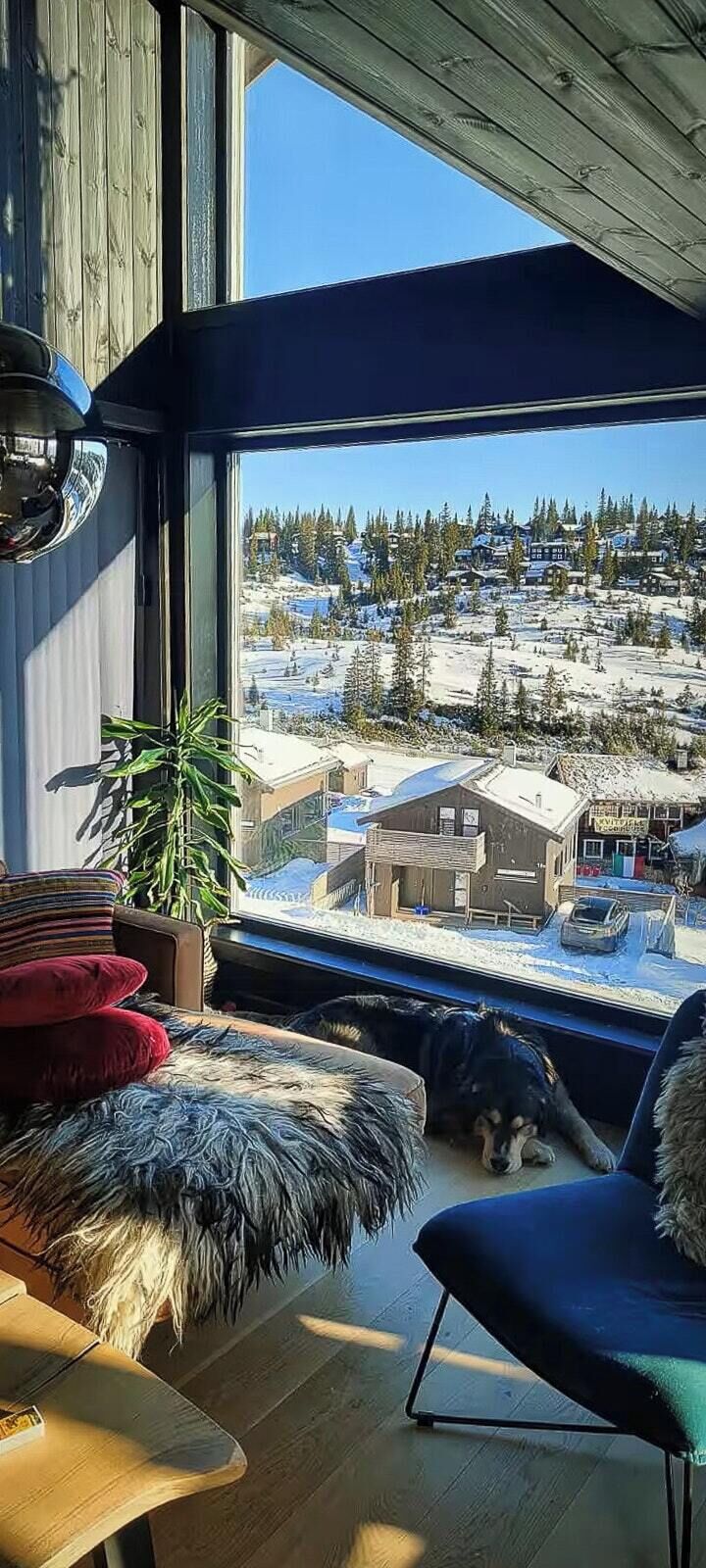 A room with a large window overlooking a snowy landscape, a wooden floor, and a blue chair.