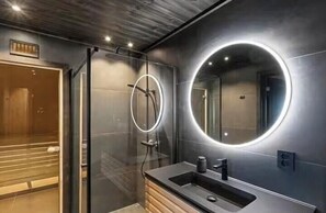 Ein modernes Badezimmer mit Duschkabine aus Glas, einem runden Spiegel mit integrierter Beleuchtung und einem Holzwaschtisch.
