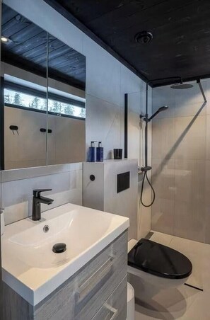 Et moderne badeværelse med et stort spejl, en hvid vask, en bruser og et toilet.
