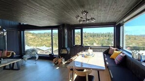 Moderni sisustus, jossa on ruokailutila, oleskelualue ja suuret ikkunat, joista avautuu näkymä ulos.
