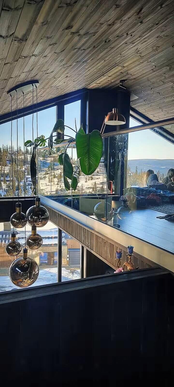 Un interior moderno con grandes ventanales, techo de madera y decoraciones esféricas colgantes.