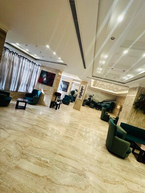 A spacious lobby with marble flooring, seating areas, and a large window with curtains.