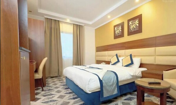 A hotel room with a bed, a desk, a chair, and a small table.