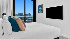 A hotel room with a large bed, a flat-screen TV, a city view, and a painting on the wall. - Luxury Apartment Perfect for Holidays on the Coast (Gold Coast)