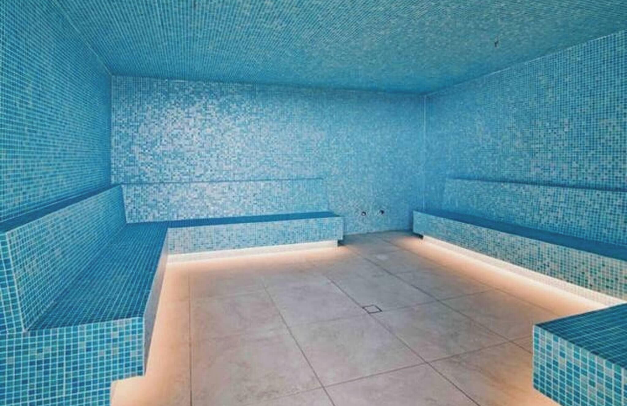 Uma piscina com paredes e chão revestidos em azulejo, bancos nas laterais e um aparelho de iluminação no teto.