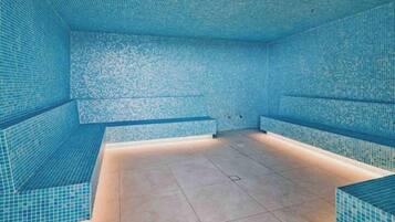 Uma piscina com paredes e chão revestidos em azulejo, bancos nas laterais e um aparelho de iluminação no teto.