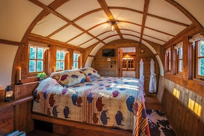 A cozy, rustic bedroom with a large bed, wooden walls, and a vaulted ceiling. - Romantic Covered Wagon w/ Hot Tub & Sauna (Murray)