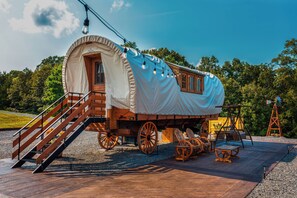 Een overdekte wagen met een houten loopplank en zitgedeelte, geplaatst op een houten terras.