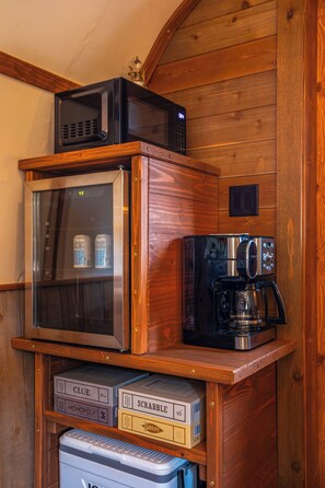 A wooden cabinet with a microwave, coffee maker, and board games. - Romantic Covered Wagon w/ Hot Tub & Sauna (Murray)
