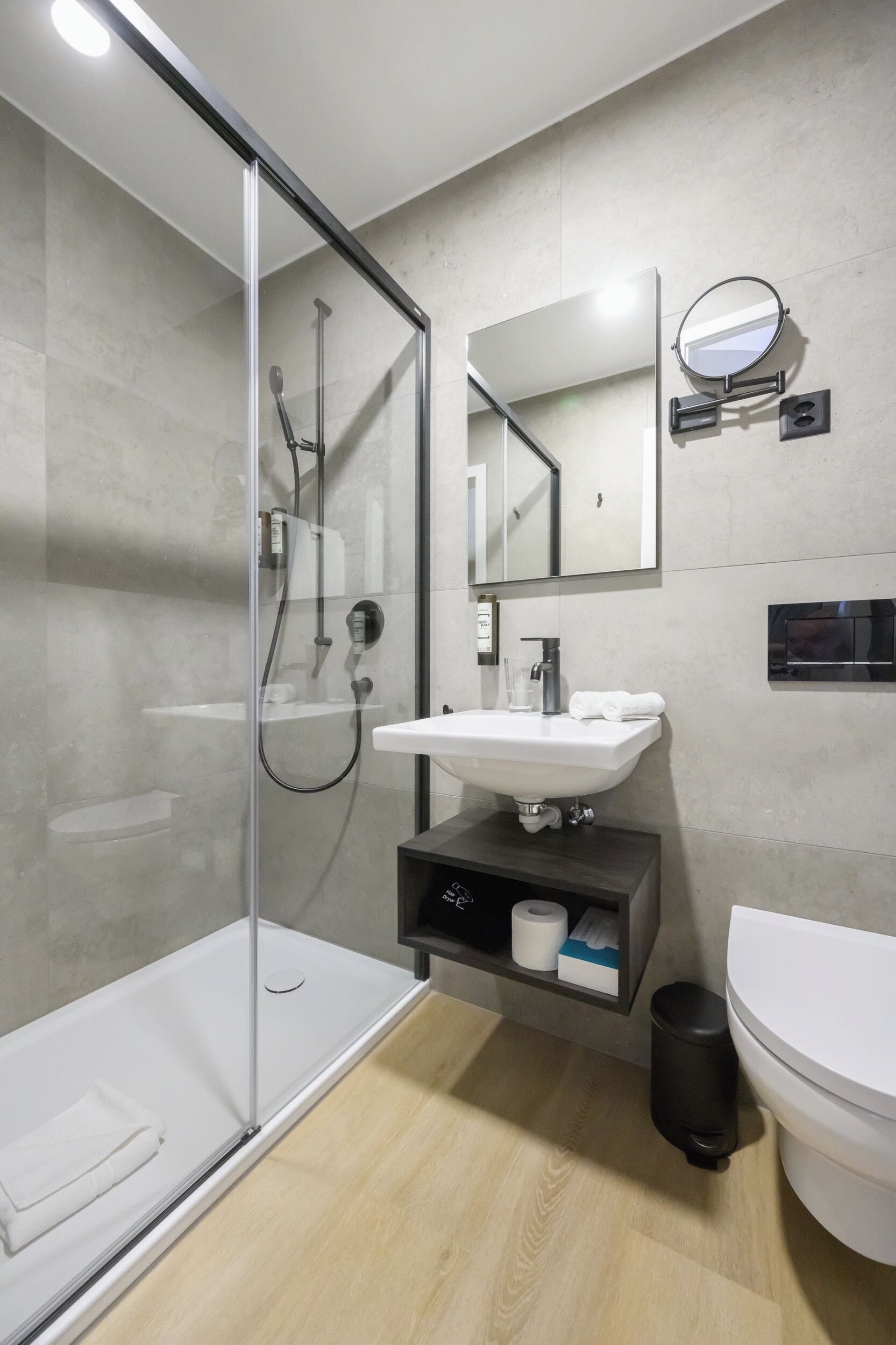 Ein modernes Badezimmer mit einer Duschkabine aus Glas, einem weißen Waschbecken, einem Spiegel und einer Toilette.