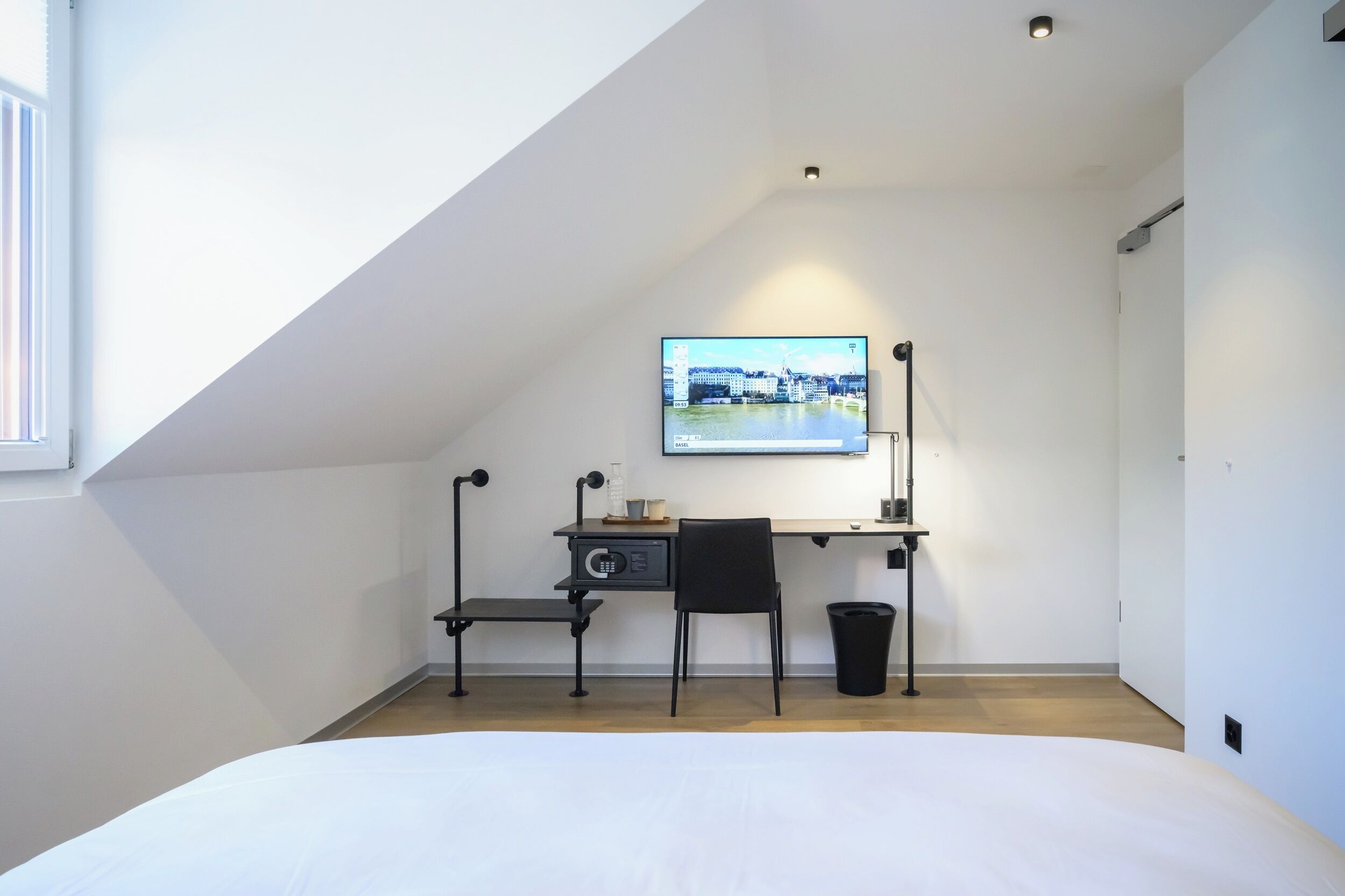 Un dormitorio moderno con techo inclinado, una cama, un escritorio con silla y un televisor montado en la pared.