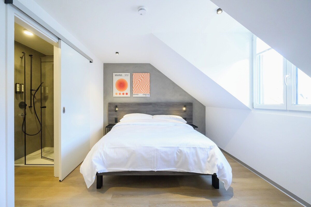 Ein modernes Schlafzimmer mit einem Bett, einer Dusche und einem großen Fenster.