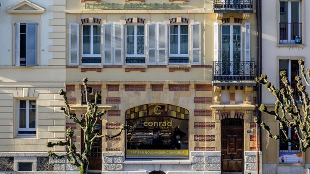 Ein mehrstöckiges Gebäude mit einem Restaurant im Erdgeschoss namens 'Conrad' und einem Hotel namens 'Hotel Arnoldo & Co.' im zweiten Stock.