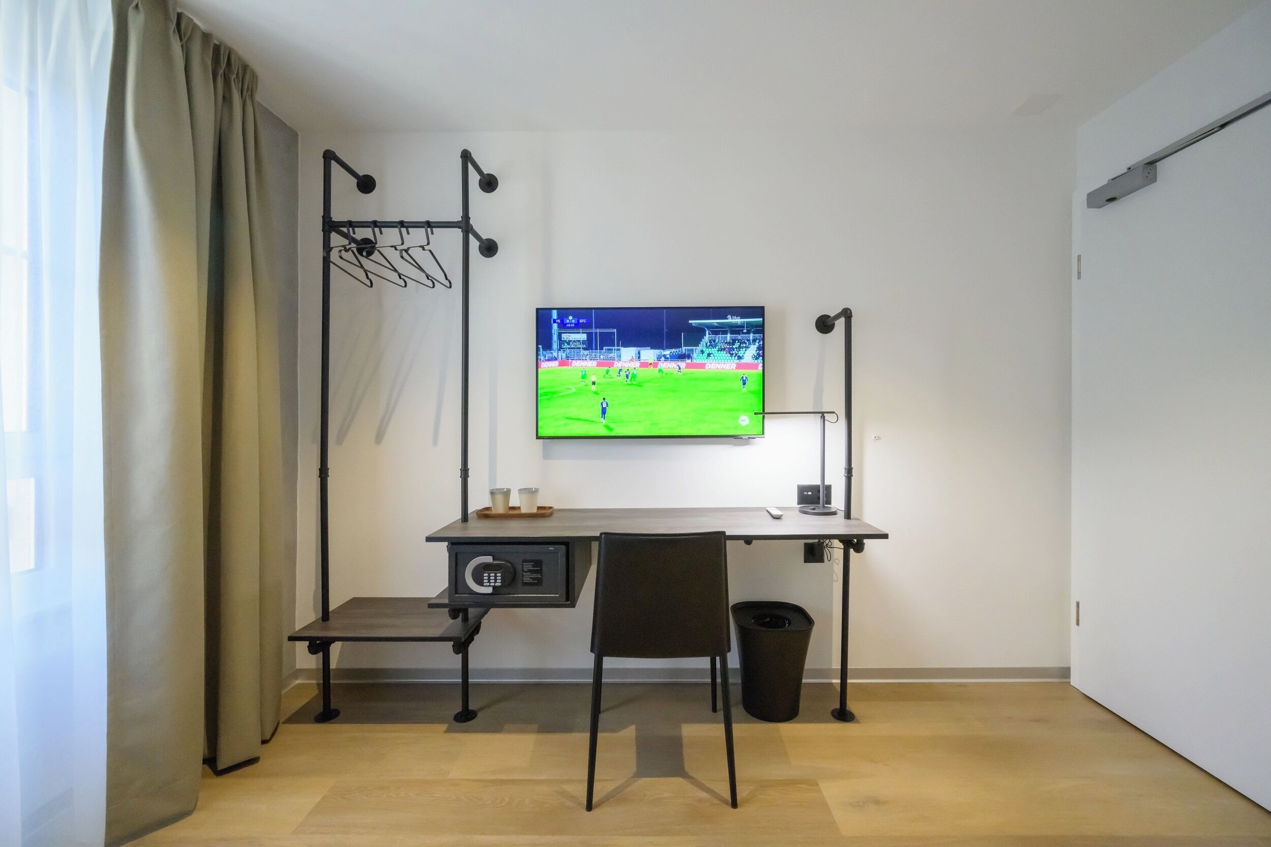 Ein kleines Zimmer mit Schreibtisch, Stuhl, Fernseher und einem kleinen Mülleimer.