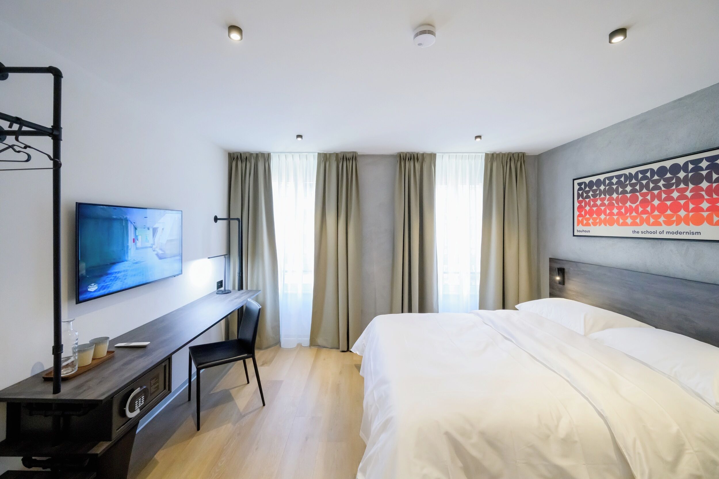 Ein Hotelzimmer mit Bett, Schreibtisch mit Fernseher, Stuhl und einem Fenster mit Vorhängen.