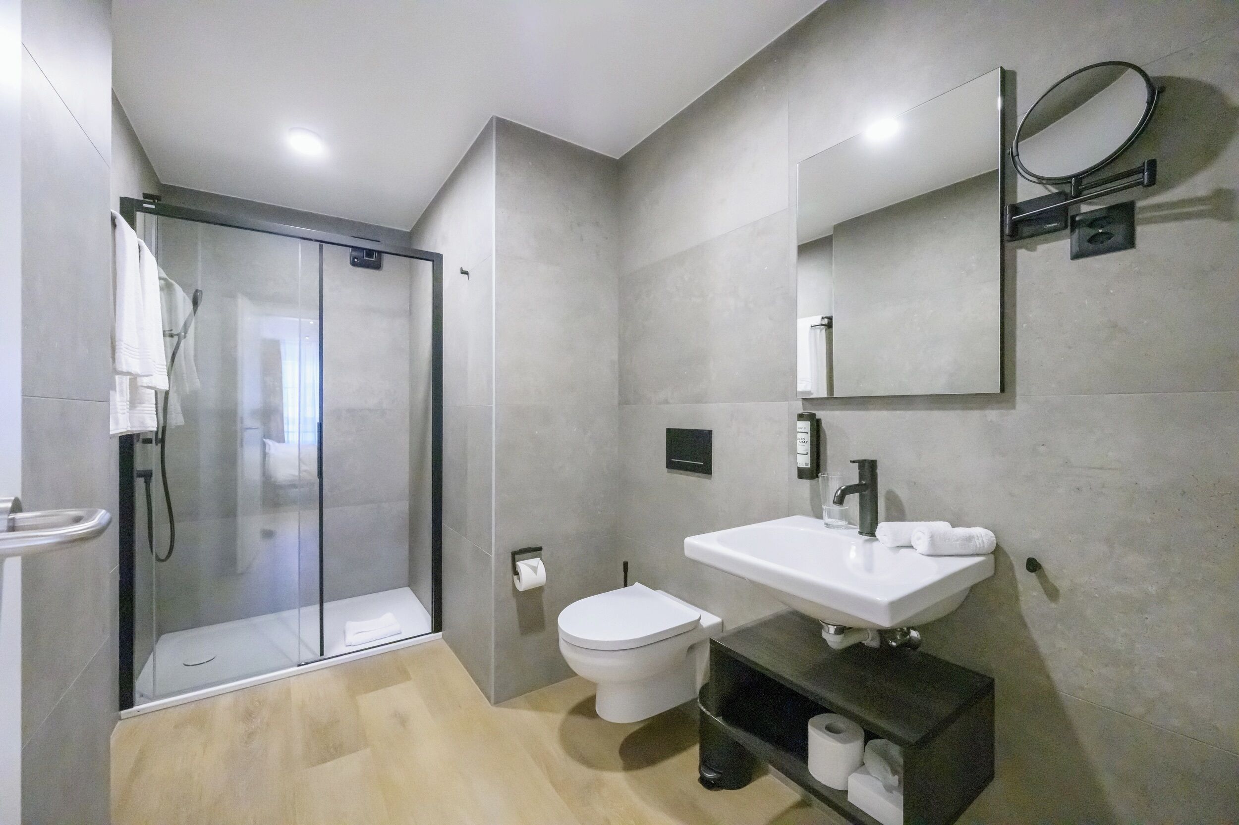 Un baño moderno con ducha envuelta en vidrio, inodoro blanco, lavamanos con espejo y tocador oscuro.