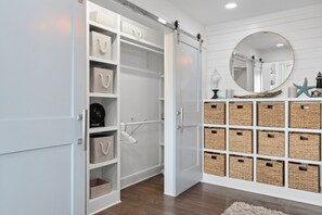 Un dressing avec des portes ouvertes, des étagères avec des boîtes de rangement, une tringle à vêtements et un mur miroir agrémenté d’objets décoratifs.
