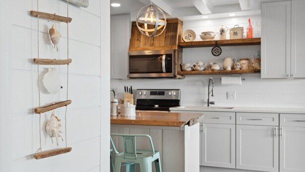 Une cuisine avec des meubles blancs, un plan de travail en bois, un luminaire suspendu et un tabouret de bar.